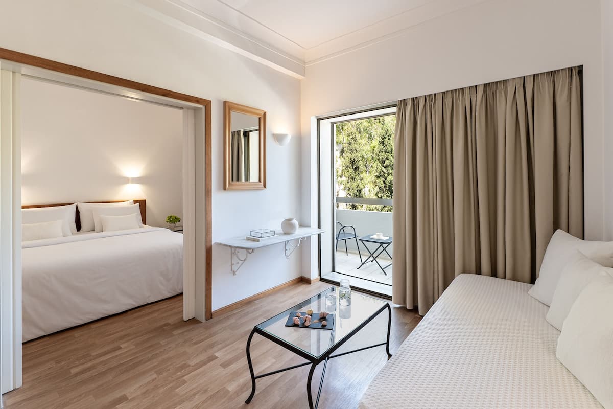 Ein Hotelzimmer mit Bett, einer Couch, einem kleinen Tisch mit Glasplatte, einem Nachttisch, einem Spiegel und einem Fenster mit Vorhängen.