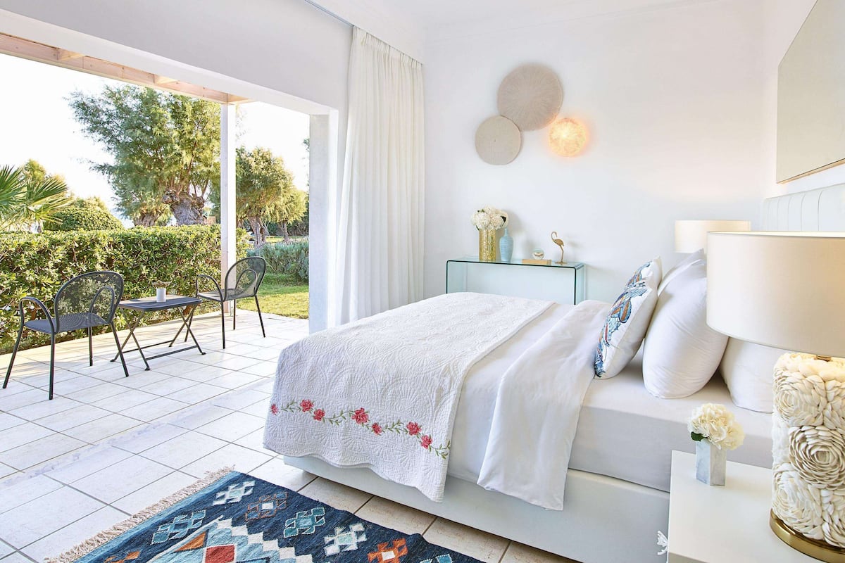 Ein Schlafzimmer mit Bett, Nachttisch und Blick auf eine Terrasse mit Stühlen und Tisch.
