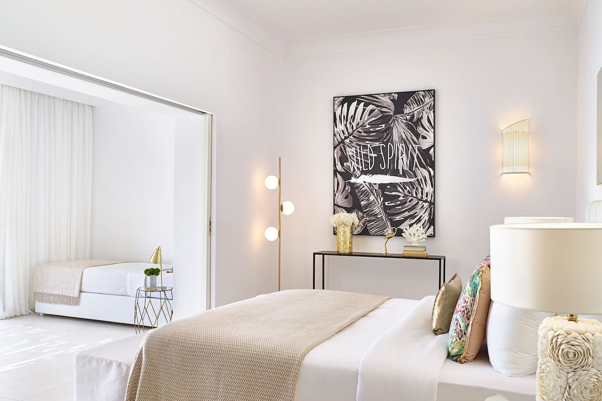 Ein modernes Schlafzimmer mit einem großen Bett, Nachttischen, einer Wandleuchte und einem großen abstrakten Kunstwerk.