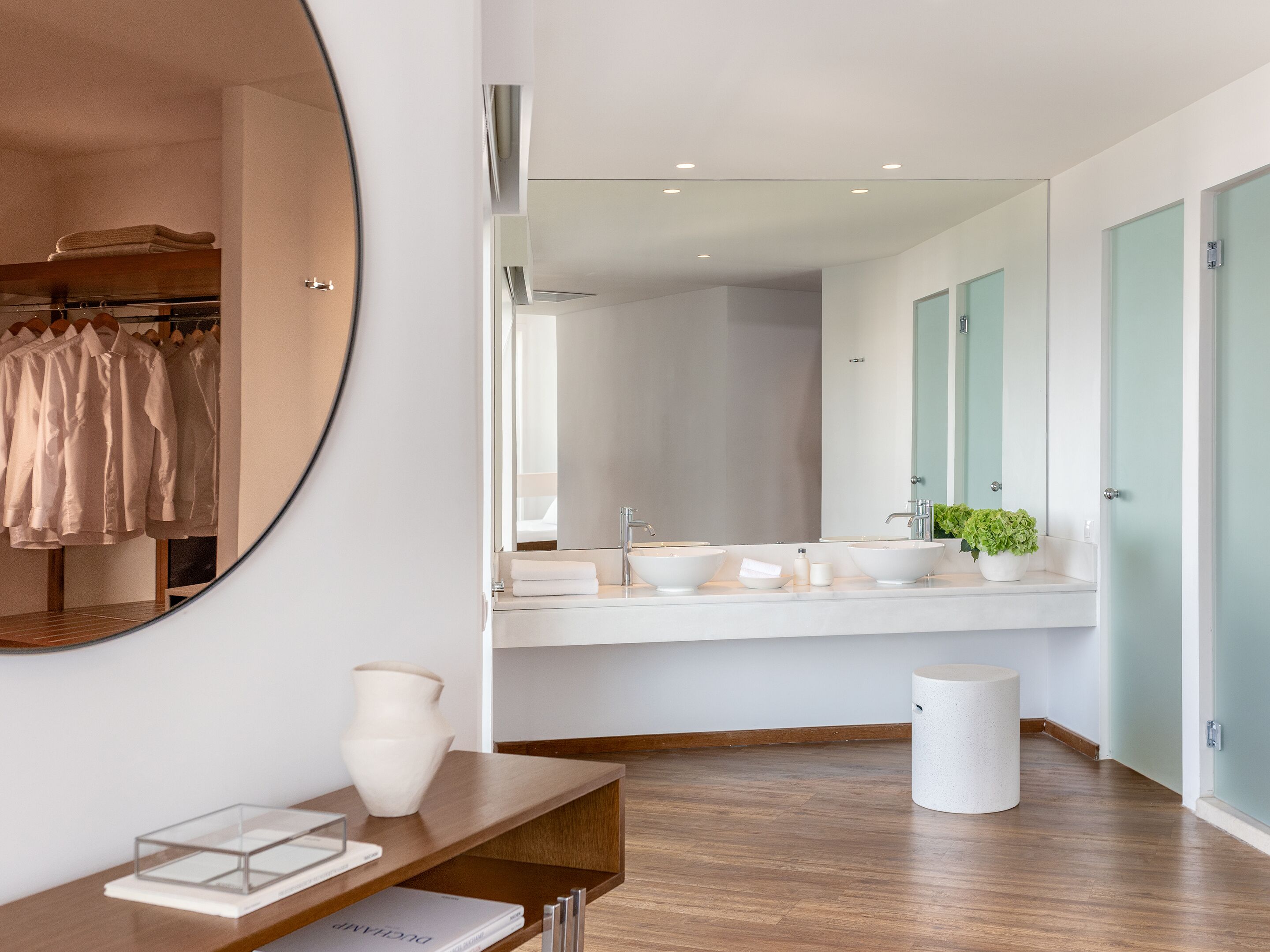 Een moderne badkamer met een grote spiegel, twee wastafels en een ronde spiegel aan de muur.