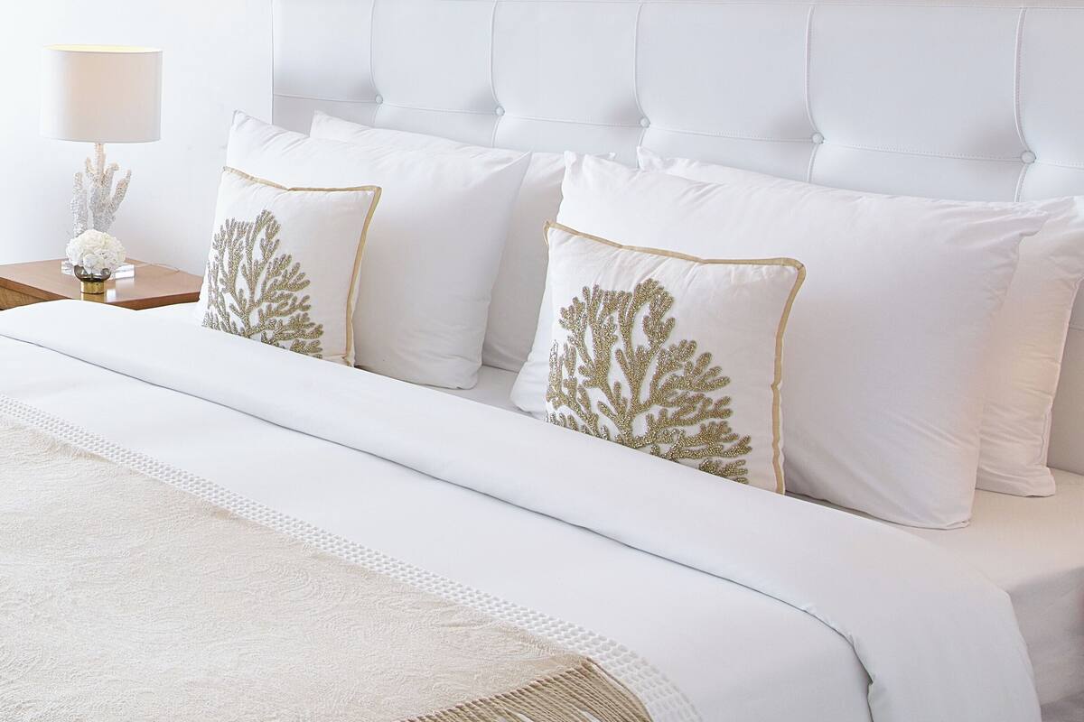 Ein ordentlich gemachtes Bett mit weißer Bettwäsche und dekorativen Kissen mit Goldstickerei.