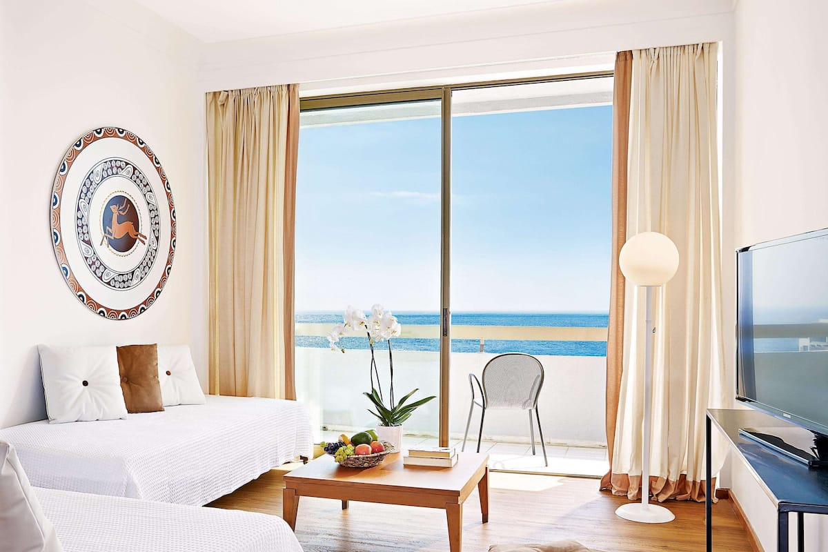 Ein Hotelzimmer mit einem Bett, einem Tisch mit Früchten, einem Sessel am Fenster und einem Fernseher.