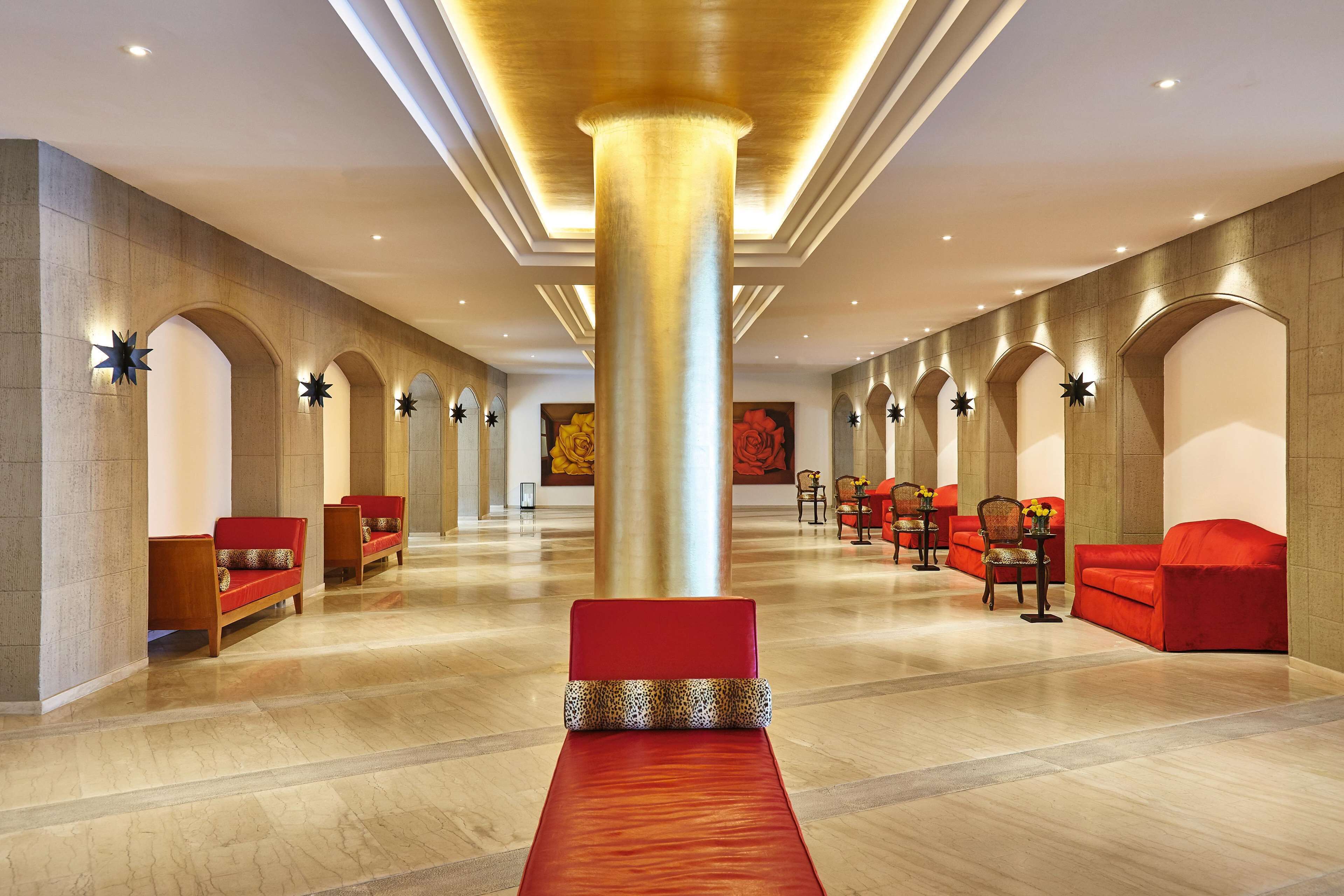 A spacious lobby with red sofas, a central red carpet, and a large golden pillar.