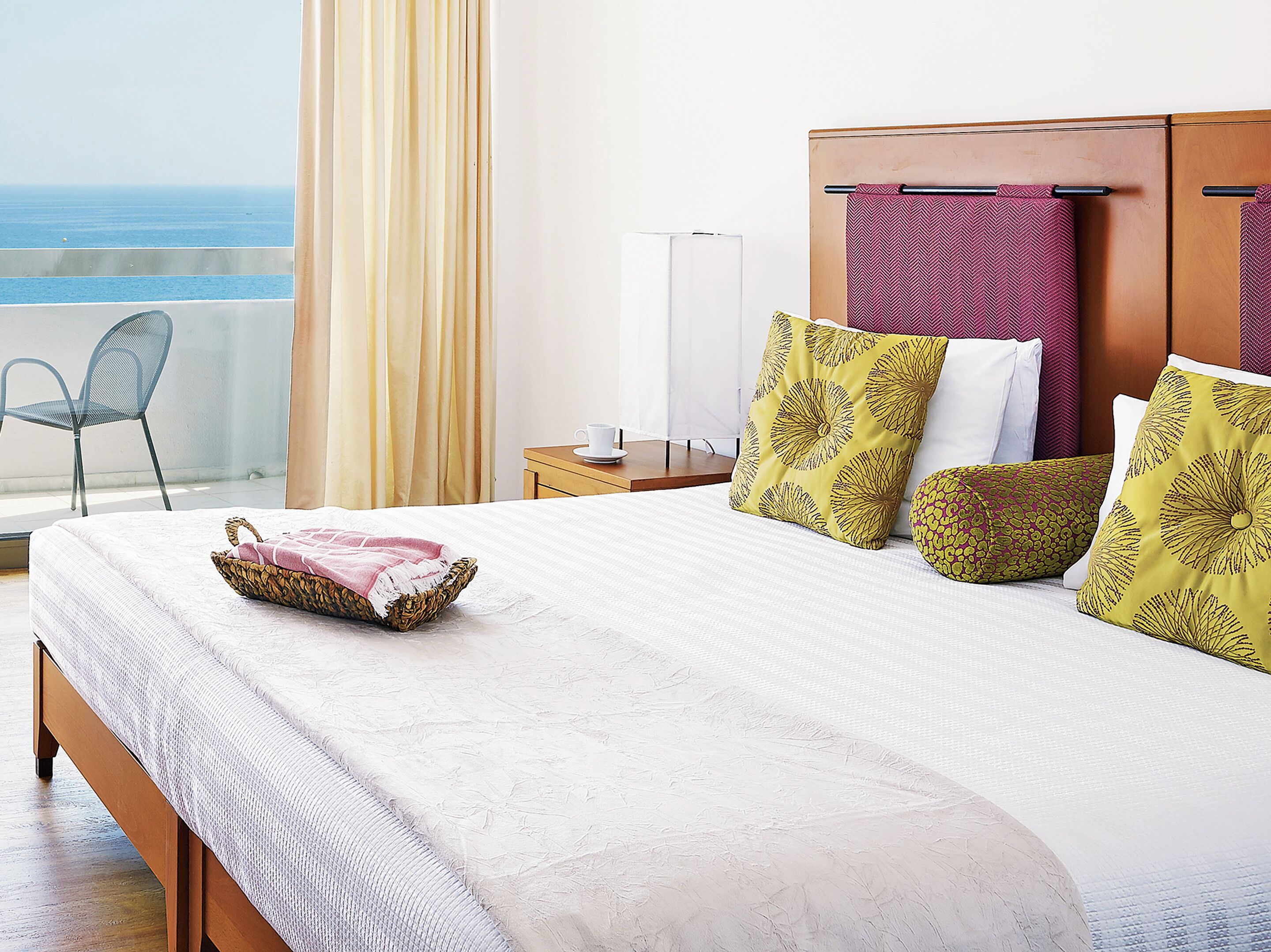 Ein Hotelzimmer mit Bett, Nachttisch, Lampe, Stuhl und Meerblick.