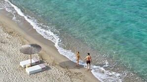 Une plage offrant une vue dégagée sur l’océan, un couple se tenant la main et un parasol de plage.