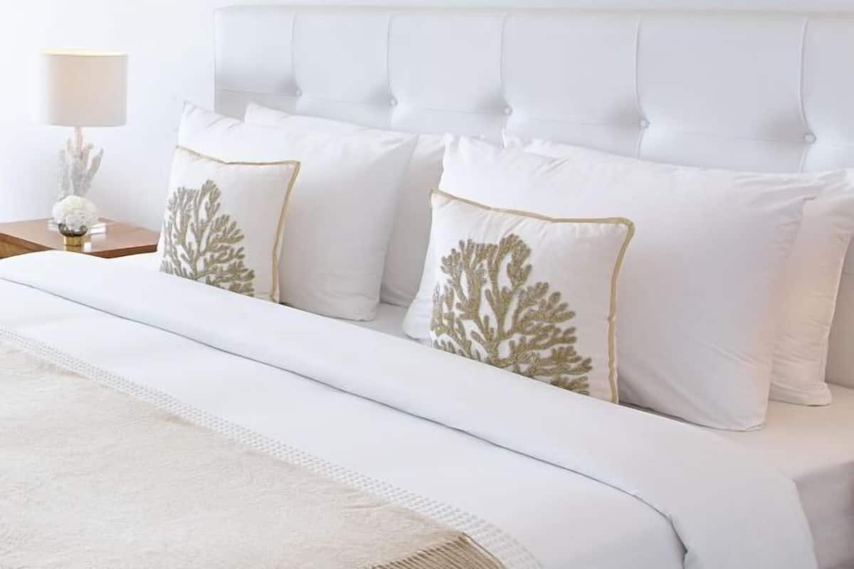 Ein Bett mit weißer Bettwäsche und dekorativen Kissen mit Goldstickerei.