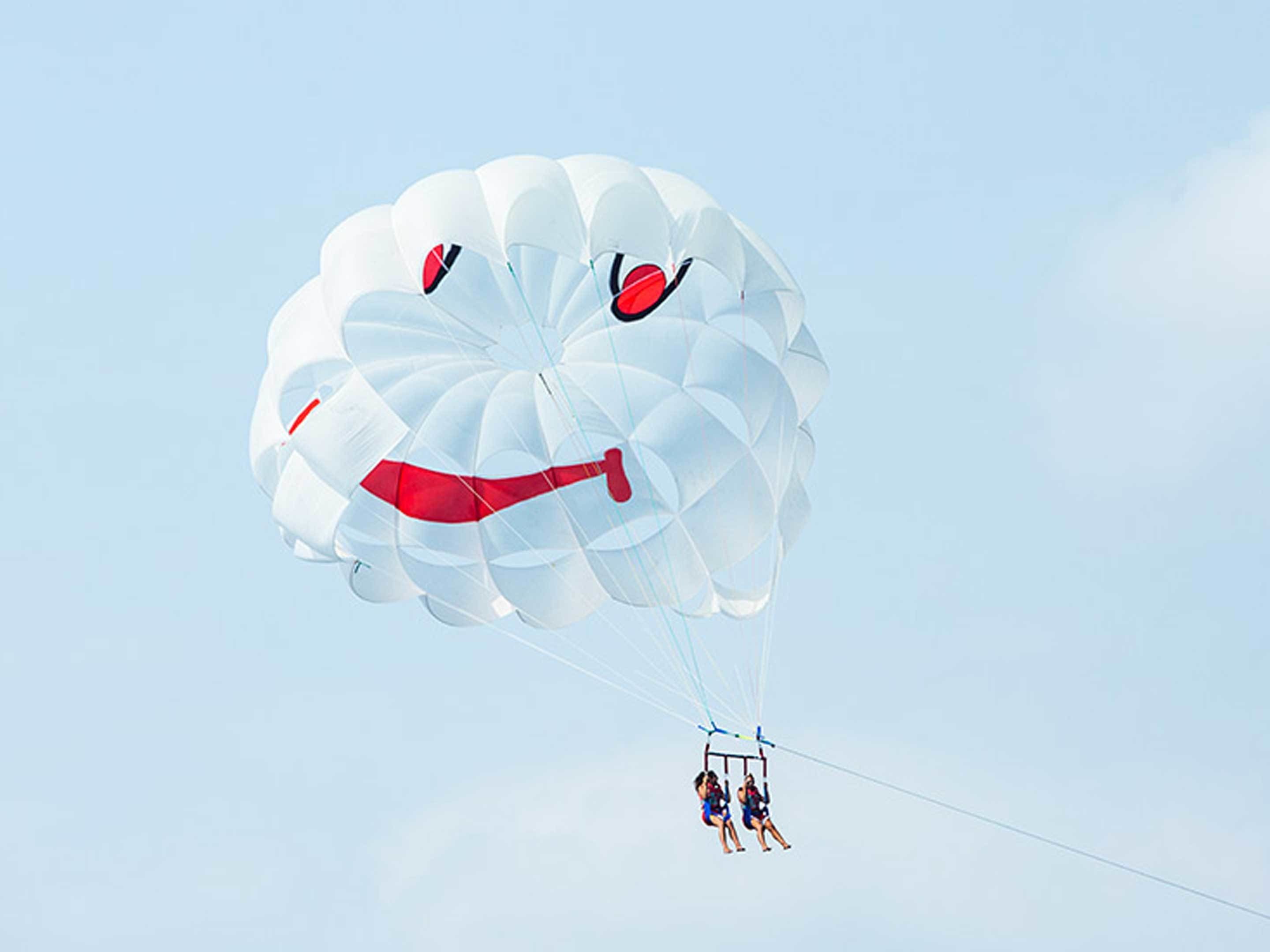 A parasail with a face design, two people in harnesses, and a clear sky.