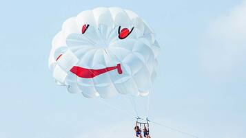 A parasail with a face design, two people in harnesses, and a clear sky.