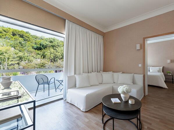 Habitación de hotel moderna con un ventanal grande, un sofá, una pequeña mesa redonda y vistas a zonas verdes.