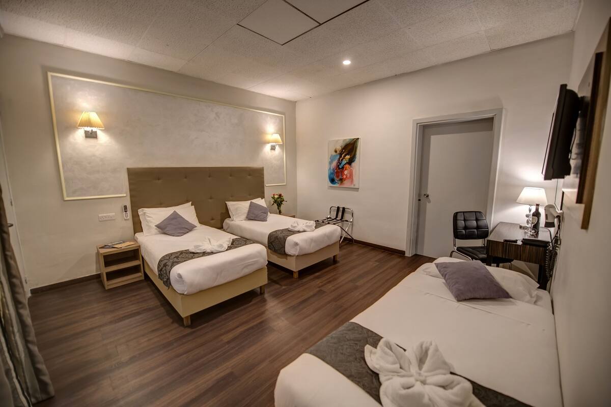 Ein Hotelzimmer mit zwei Betten, einem Schreibtisch, einem Sessel und einem Fernseher.