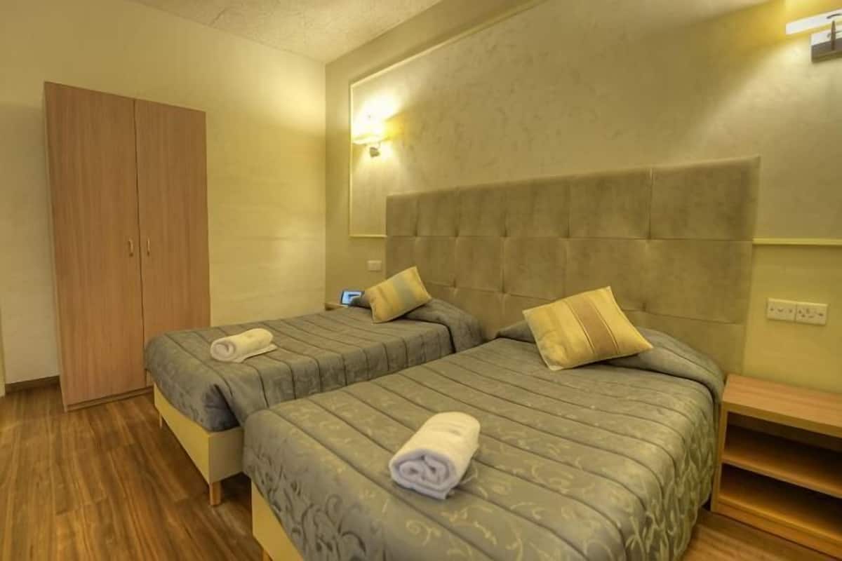 A hotel room with two beds, a wardrobe, and a bedside table.