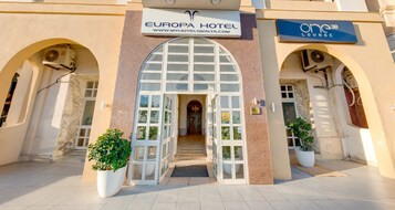 The Europa Hotel entrance with a large arched doorway, potted plants, and a sign for the One38 Lounge.
