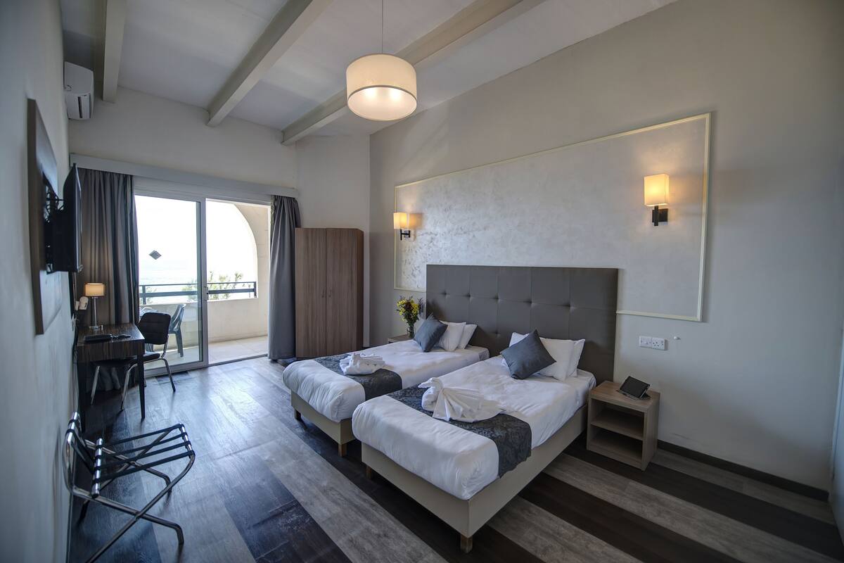 Ein Hotelzimmer mit zwei Betten, einem Schreibtisch, einem Stuhl, einem kleinen Tisch und einer Deckenleuchte.