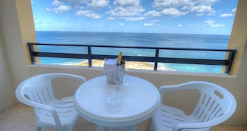 A balcony with a table and two chairs, overlooking a beach and the ocean.