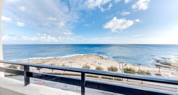 Vista costera desde un balcón con barandilla, que da a una playa y al mar.