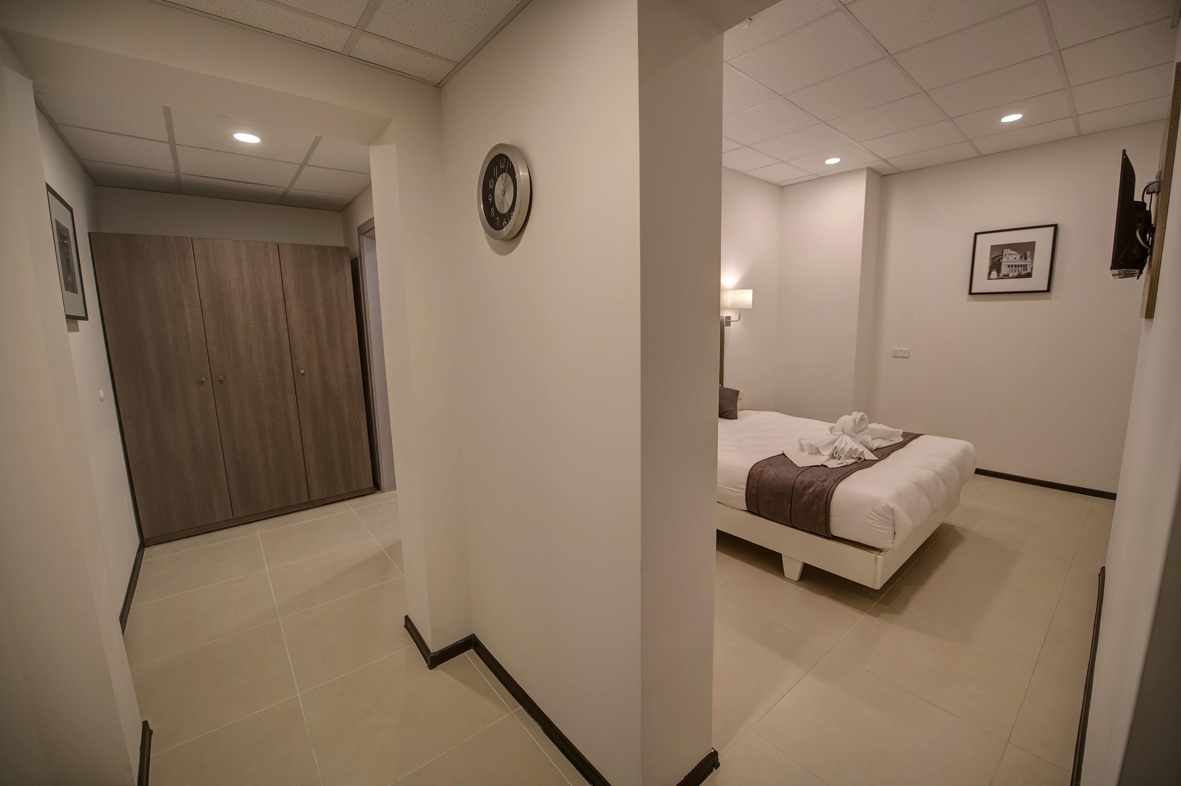 Une chambre d’hôtel avec un lit, une horloge au mur et un tableau encadré.