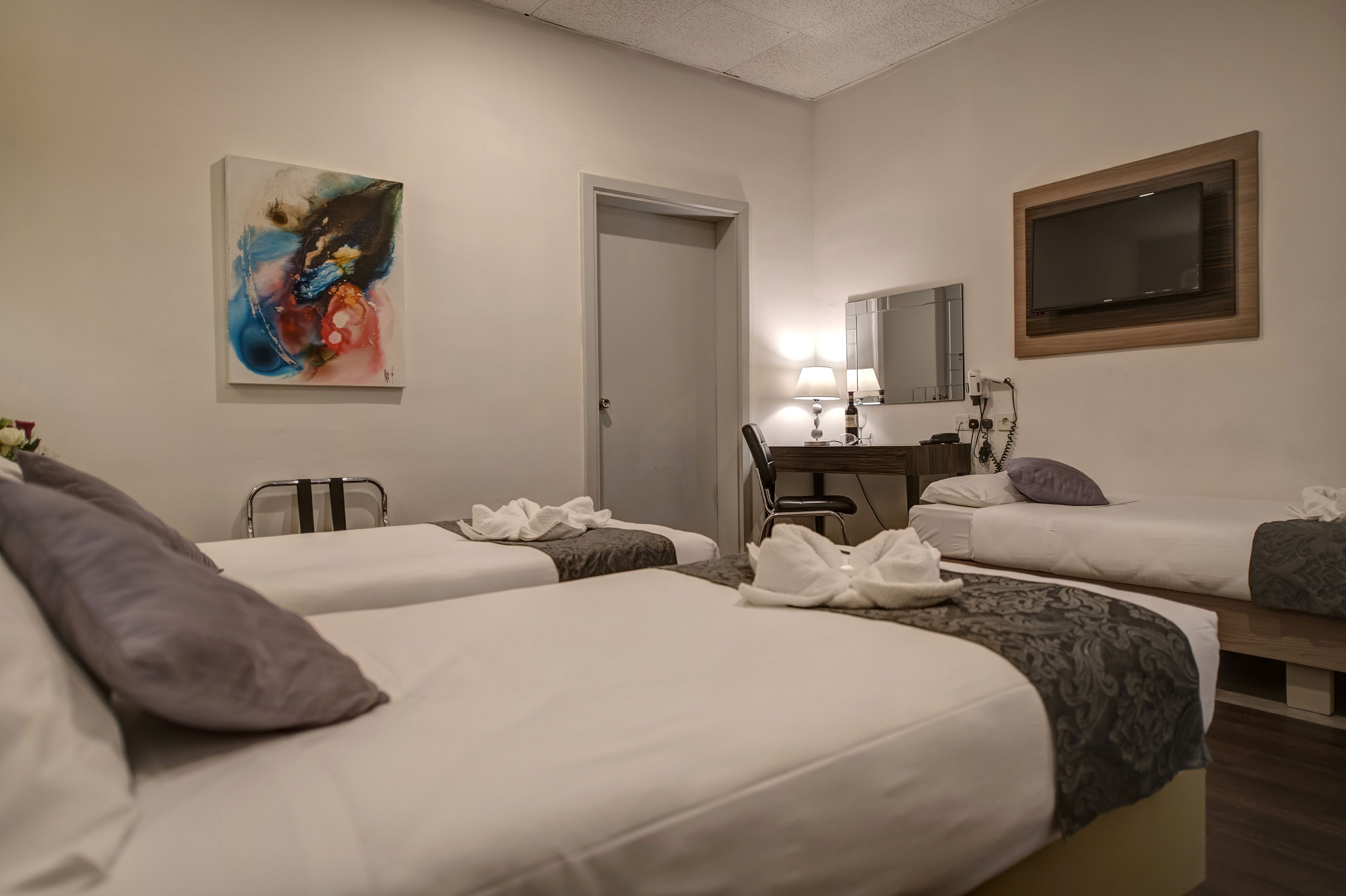 A hotel room with two beds, a desk with a lamp, a chair, a TV, and a painting on the wall.
