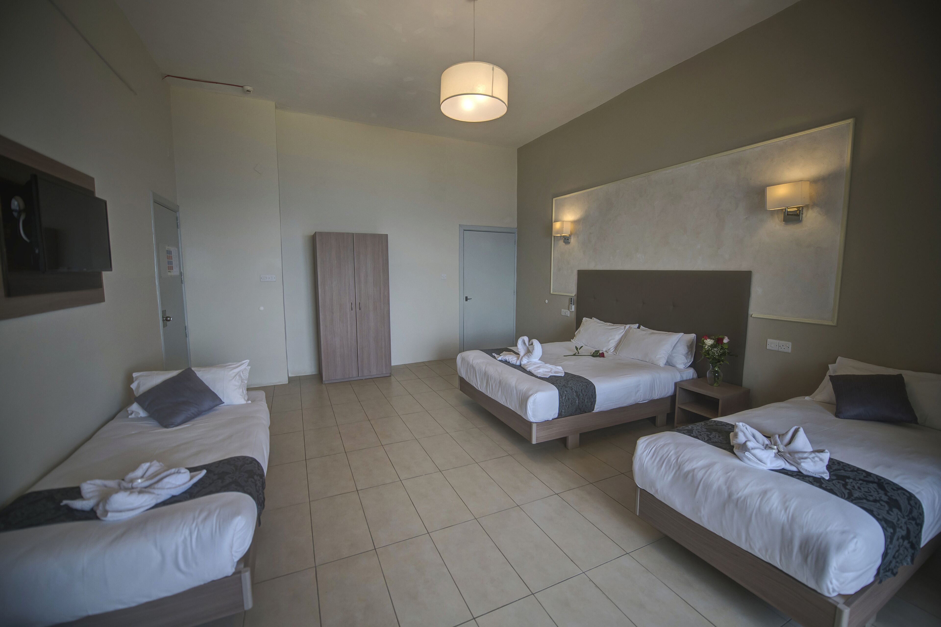 A hotel room with two single beds and a double bed, all neatly made with towels.
