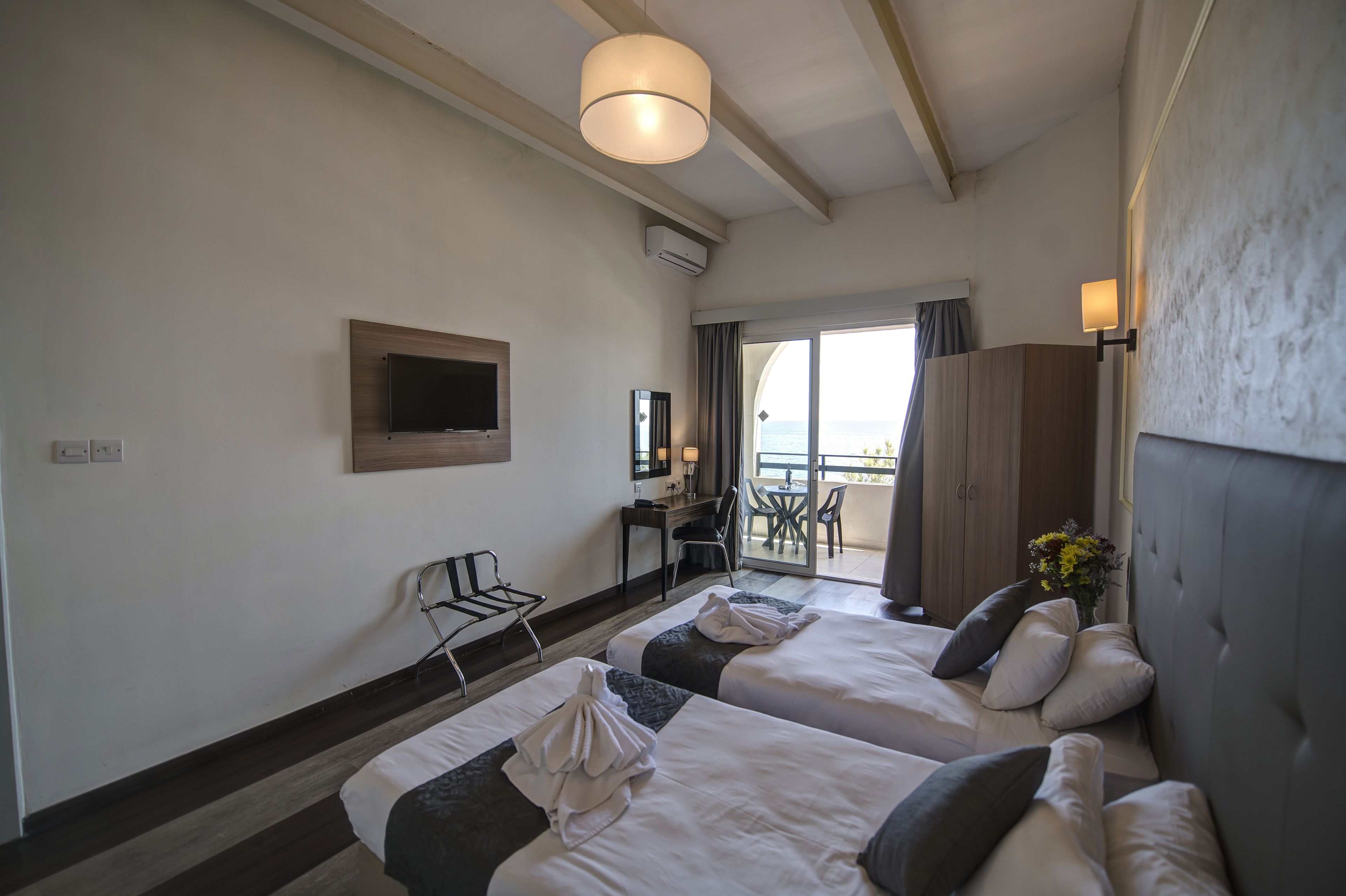 Ein Hotelzimmer mit zwei Betten, einem Schreibtisch, einem Stuhl, einem Fernseher und einem Balkon mit Blick.
