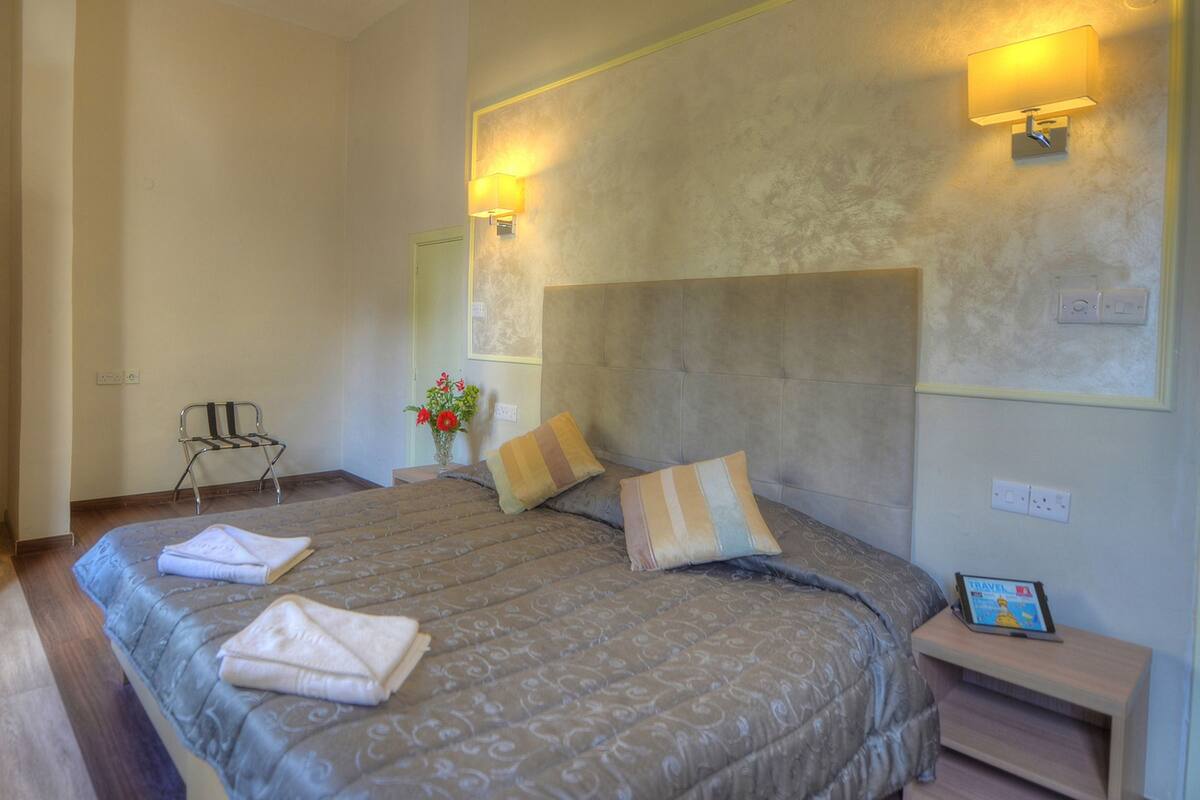 Ein Hotelzimmer mit einem großen Bett, zwei Nachttischen, einem Sessel und einer Wandlampe.