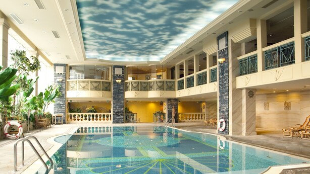 Una amplia piscina interior con un mural en el techo, varios balcones y un interior bien iluminado.
