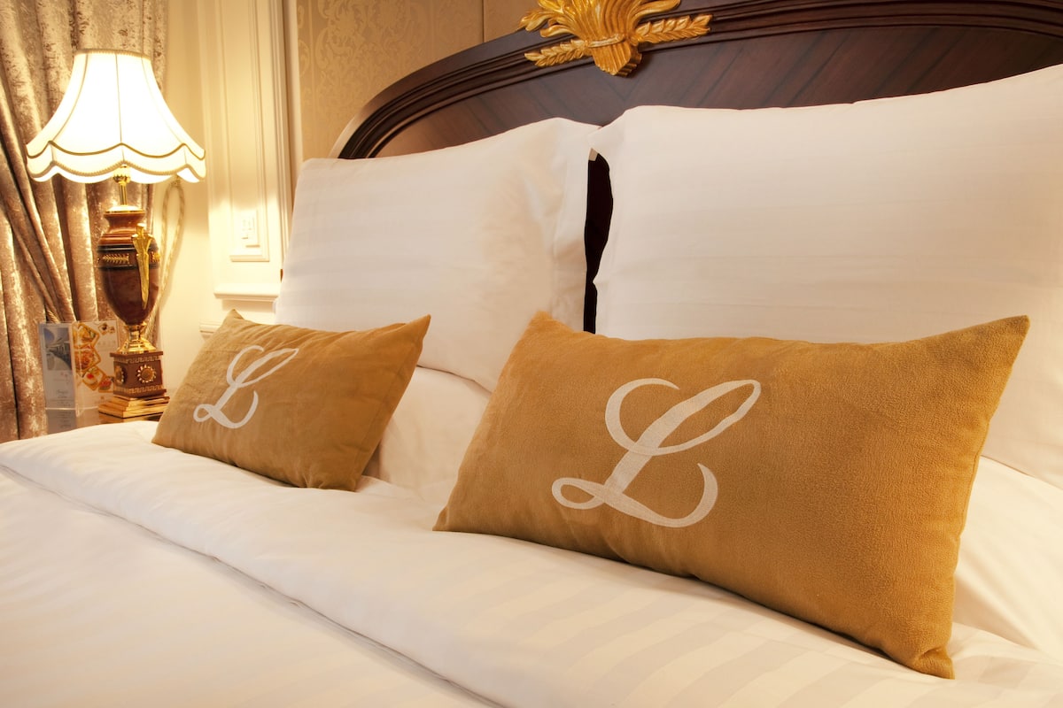 A neatly made bed with white linens and two pillows with a monogram.