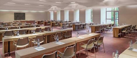 A conference room with multiple tables and chairs, equipped with water bottles and glasses, and large windows allowing natural light.