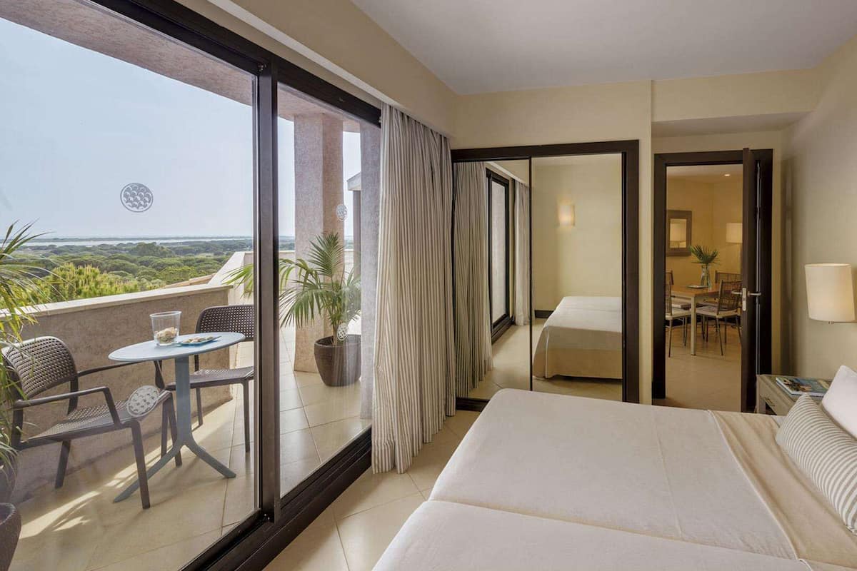 A hotel room with a balcony, a bed, a dining area, and a view of the landscape.