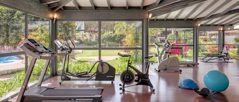Un gimnasio con cintas de correr, bicicletas estáticas y pelotas de ejercicio, con amplios ventanales y suelo de madera.