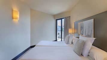 Habitación de hotel con dos camas, un ventanal con cortinas, un cuadro en la pared y una lámpara fijada a la pared.