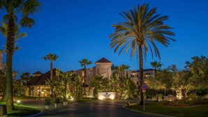 A hotel with a central building, palm trees, and a well-lit entrance.