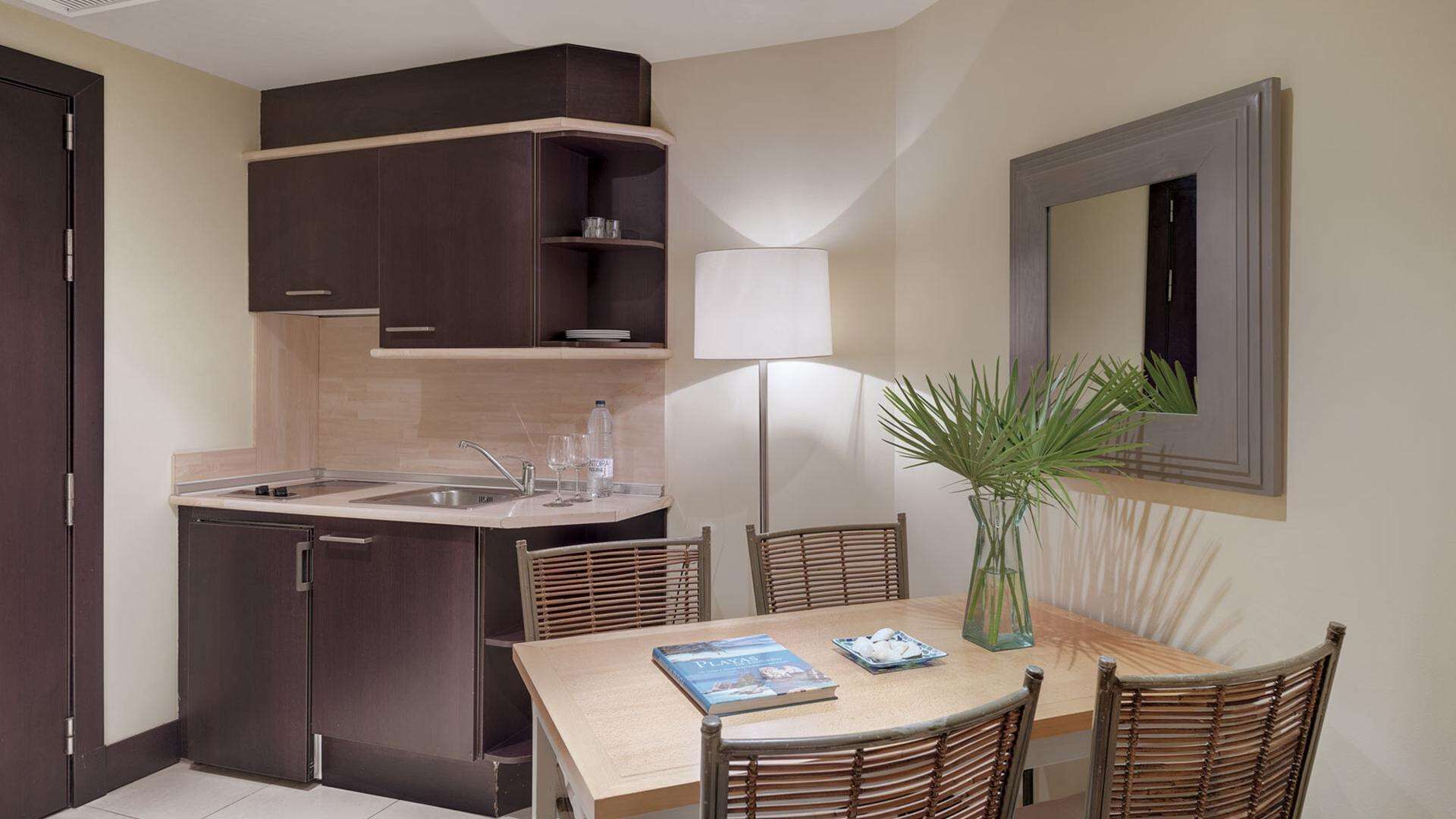 Cocina compacta con lavamanos, armarios y comedor con mesa y sillas.