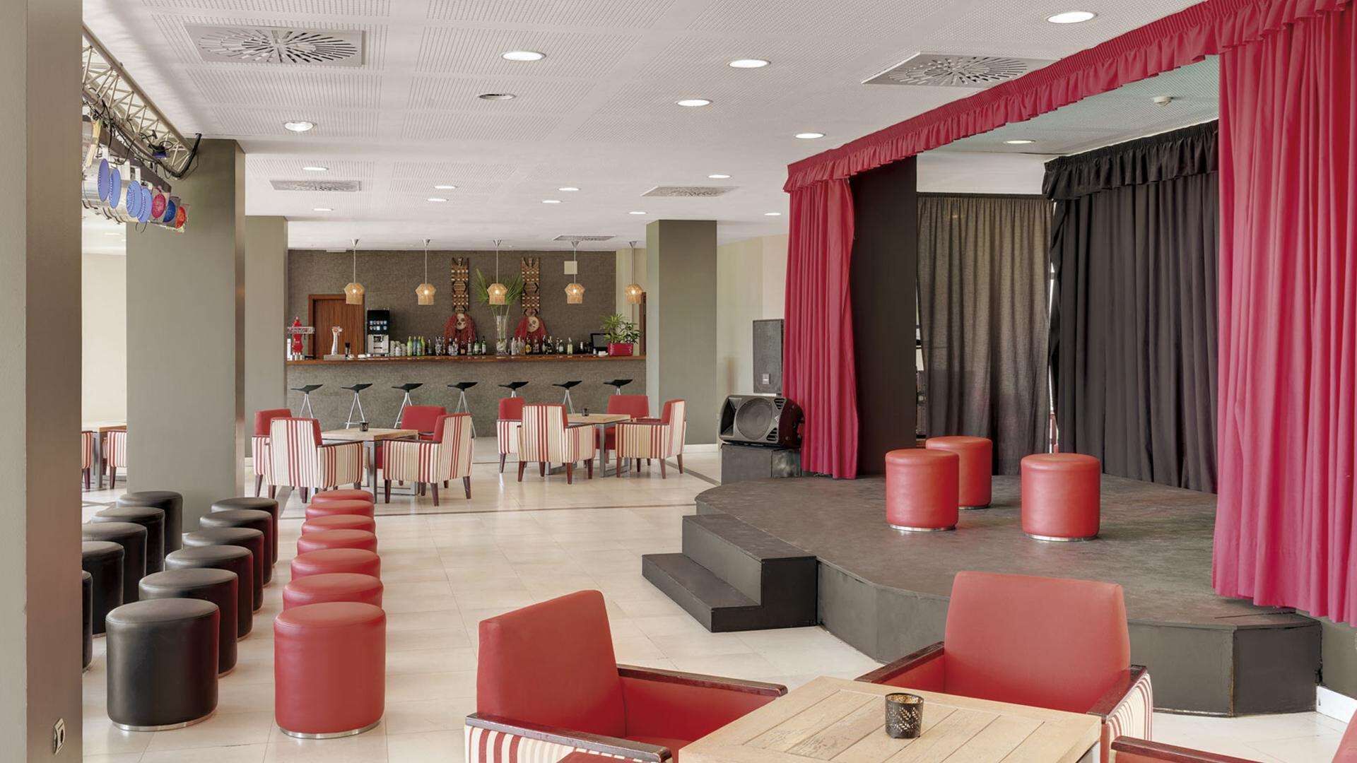 A modern hotel lobby with a bar area, seating arrangements, and a stage with curtains.