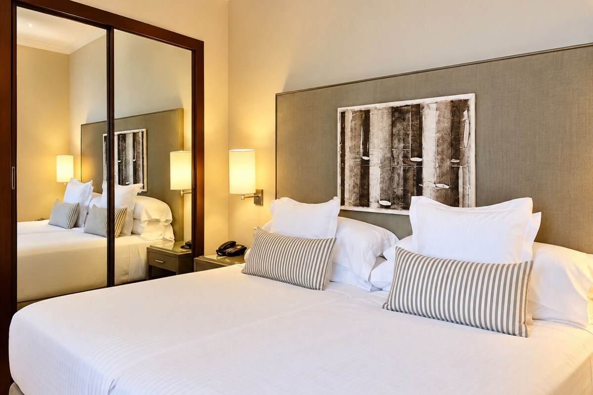 A hotel room with a large bed, two bedside tables, a mirror, and a wall-mounted artwork.