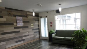 Ein Empfangsbereich mit einer Holzwand, einer Couch, einem Sessel und einer Zimmerpflanze.