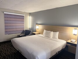 Habitación de hotel con una cama grande, un escritorio, una silla, una mesita de noche con un teléfono y una persiana con diseño.