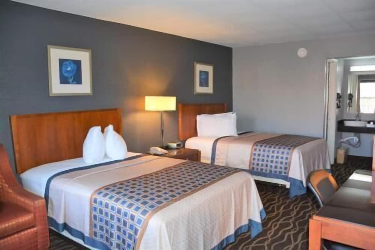 Ein Hotelzimmer mit zwei Betten, einem Schreibtisch, einem Stuhl und einem durch eine offene Tür einsehbaren Badezimmer.