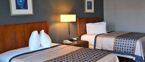 A hotel room with two beds, a nightstand, a lamp, and framed artwork on the walls.