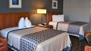Ein Hotelzimmer mit zwei Betten, einem Holzkopfteil, einem Nachttisch mit Lampe und einem gerahmten Bild an der Wand.