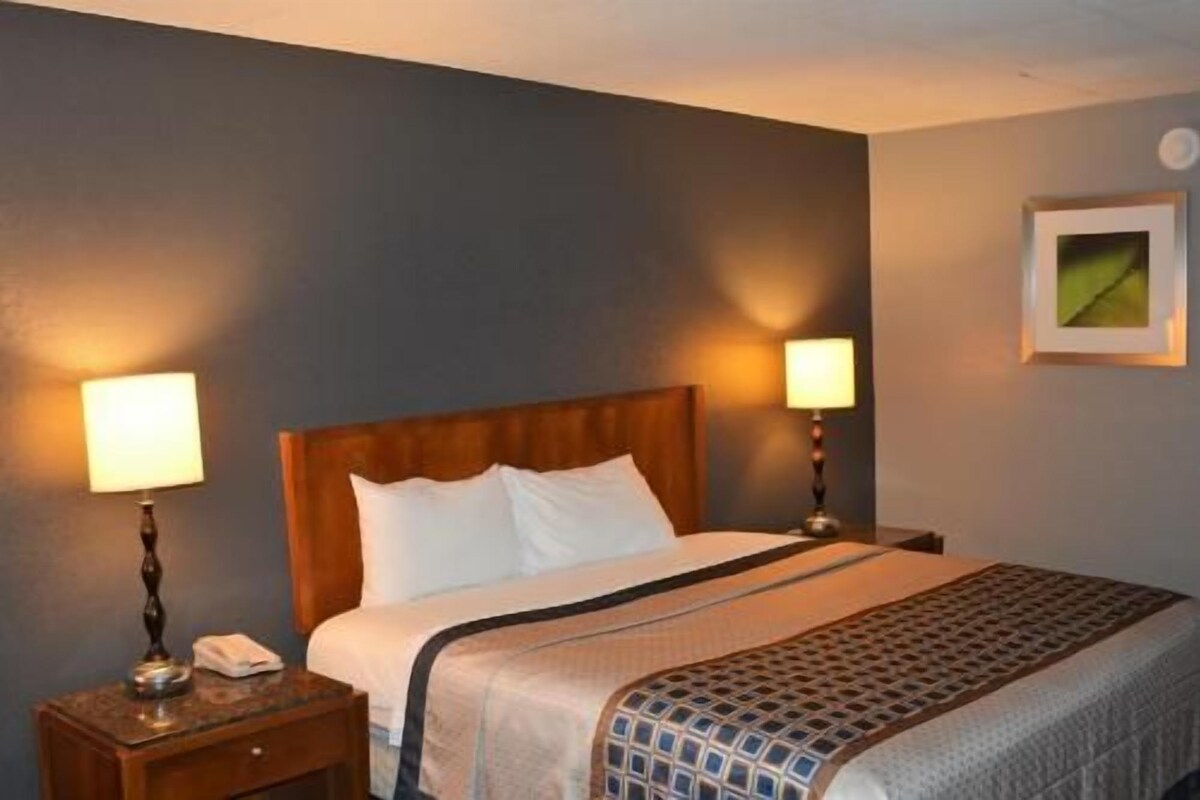 A hotel room with a bed, two bedside lamps, a nightstand with a phone, and a framed picture on the wall.