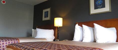 A hotel room with two beds, a nightstand, a lamp, and two framed pictures on the wall.
