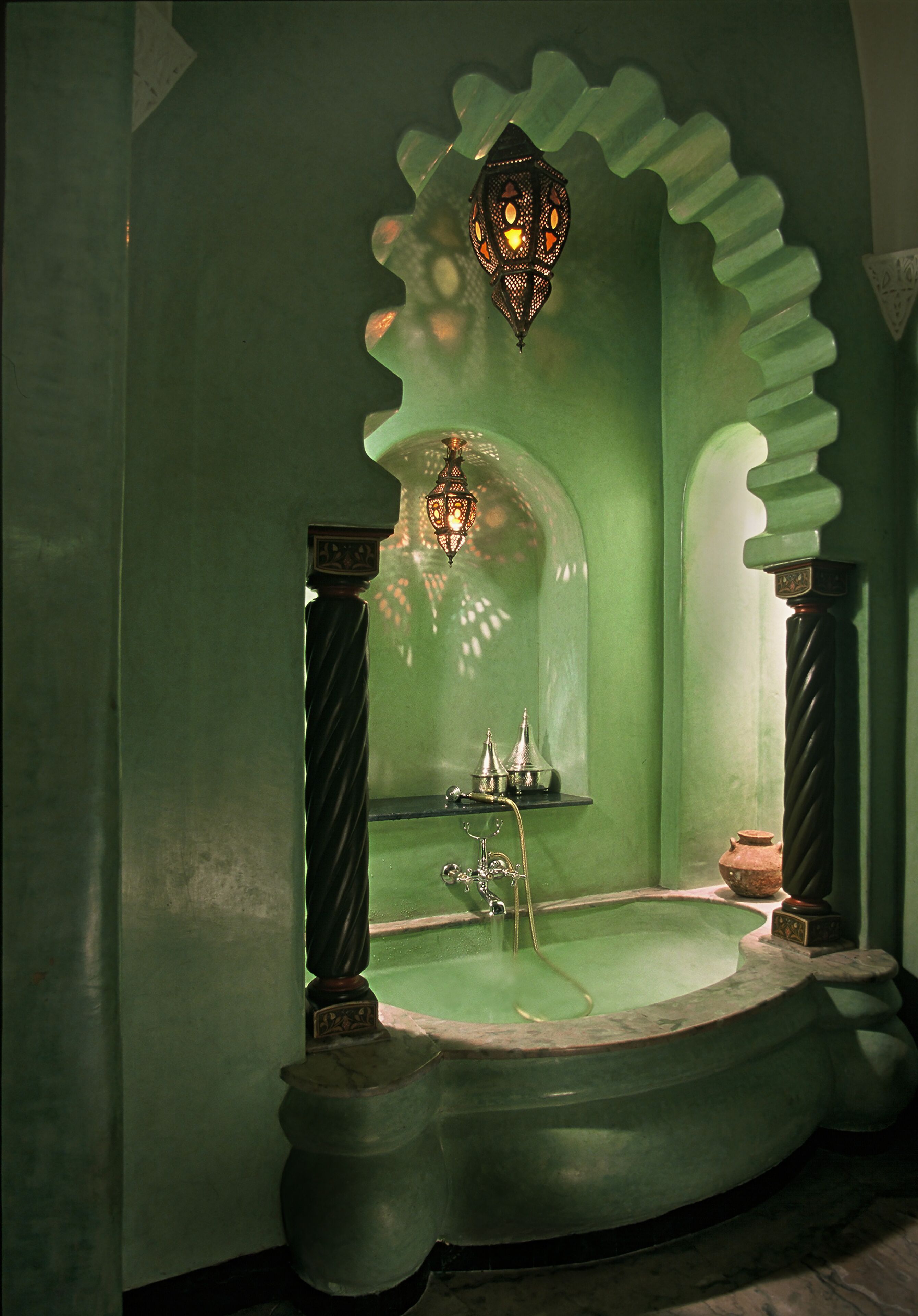 A green bathroom with a freestanding bathtub, a wall-mounted light fixture, and decorative metal elements.