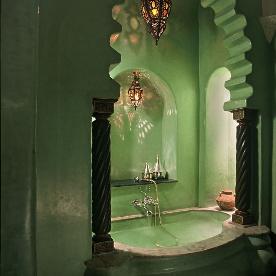 A green bathroom with a freestanding bathtub, a wall-mounted light fixture, and decorative metal elements.