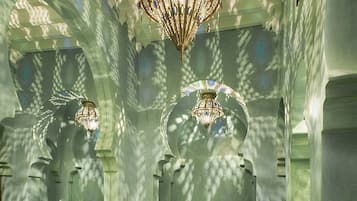 A luxurious bathroom with a large, ornate chandelier, a round marble sink, and a freestanding bathtub.