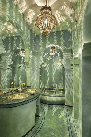 A luxurious bathroom with a large, ornate chandelier, a round marble sink, and a freestanding bathtub.
