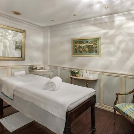 A bedroom with a bed, a chair, a vanity, and two framed artworks on the wall.