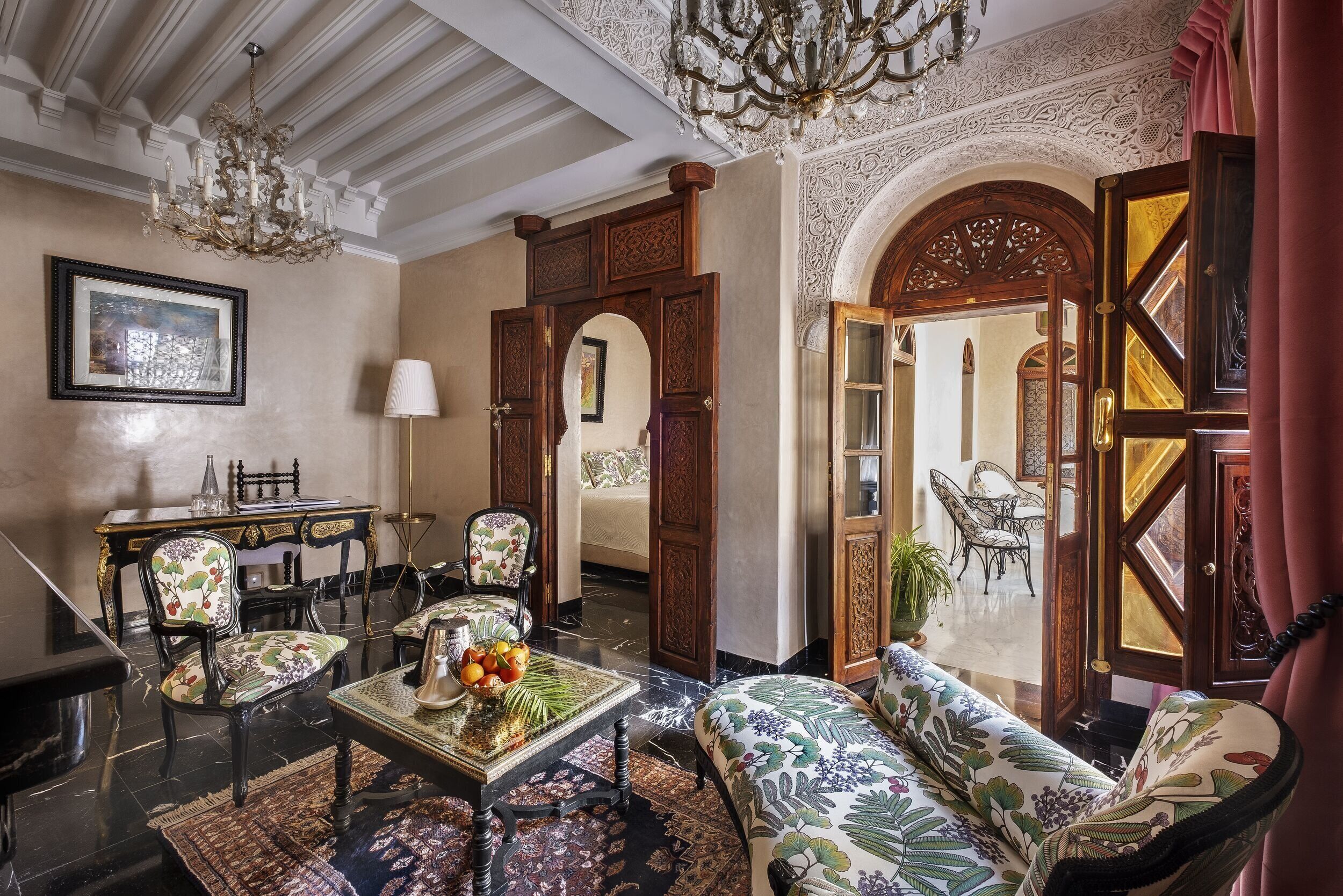A luxurious living room with ornate woodwork, a chandelier, and a sofa with floral upholstery.