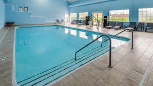 An indoor swimming pool with clear water, tiled floor, and a blue wall. There are lounge chairs and a staircase leading to an upper level. - Baymont by Wyndham Beulah (Beulah)