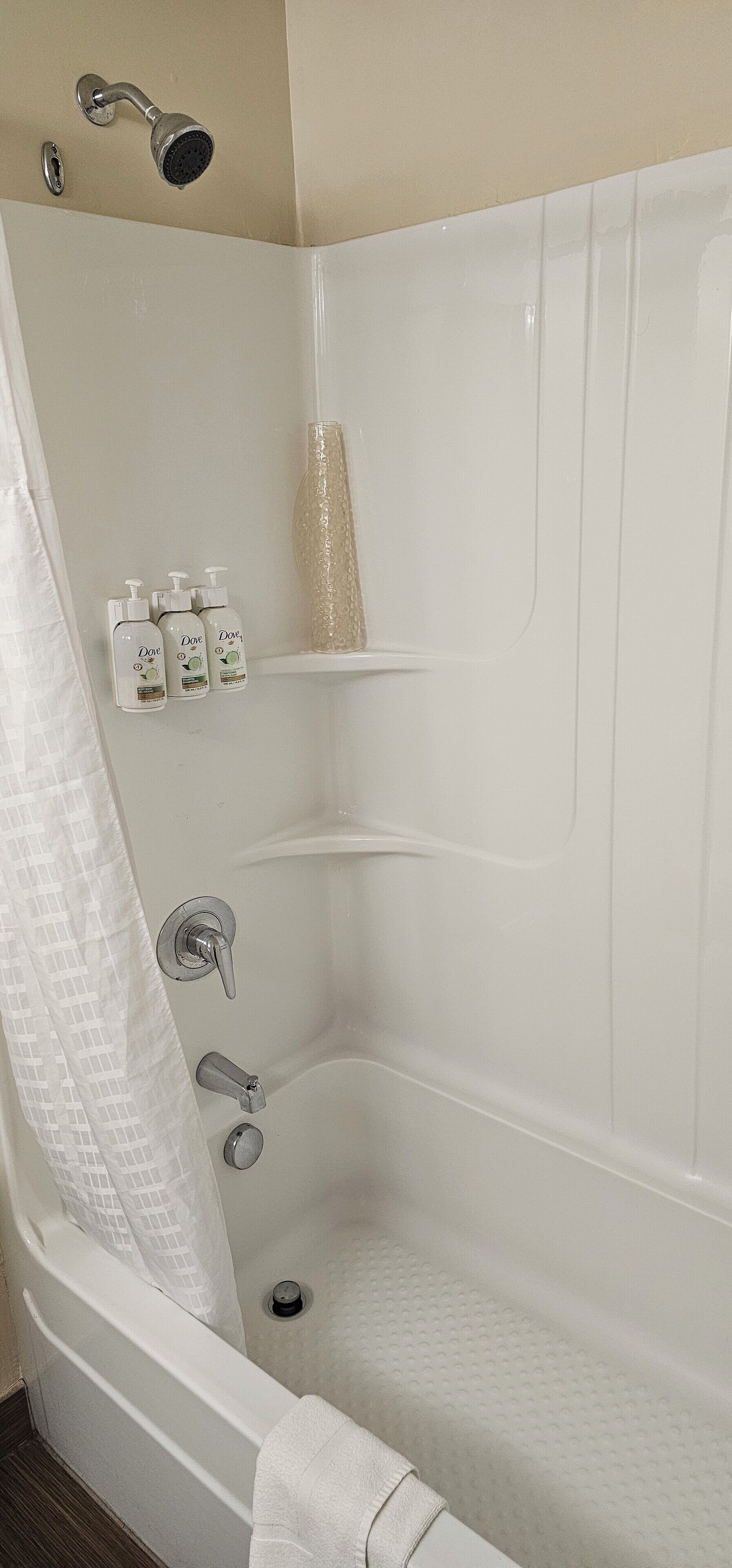 A bathroom with a bathtub, shower, and three bottles of Dove body wash on a shelf.
