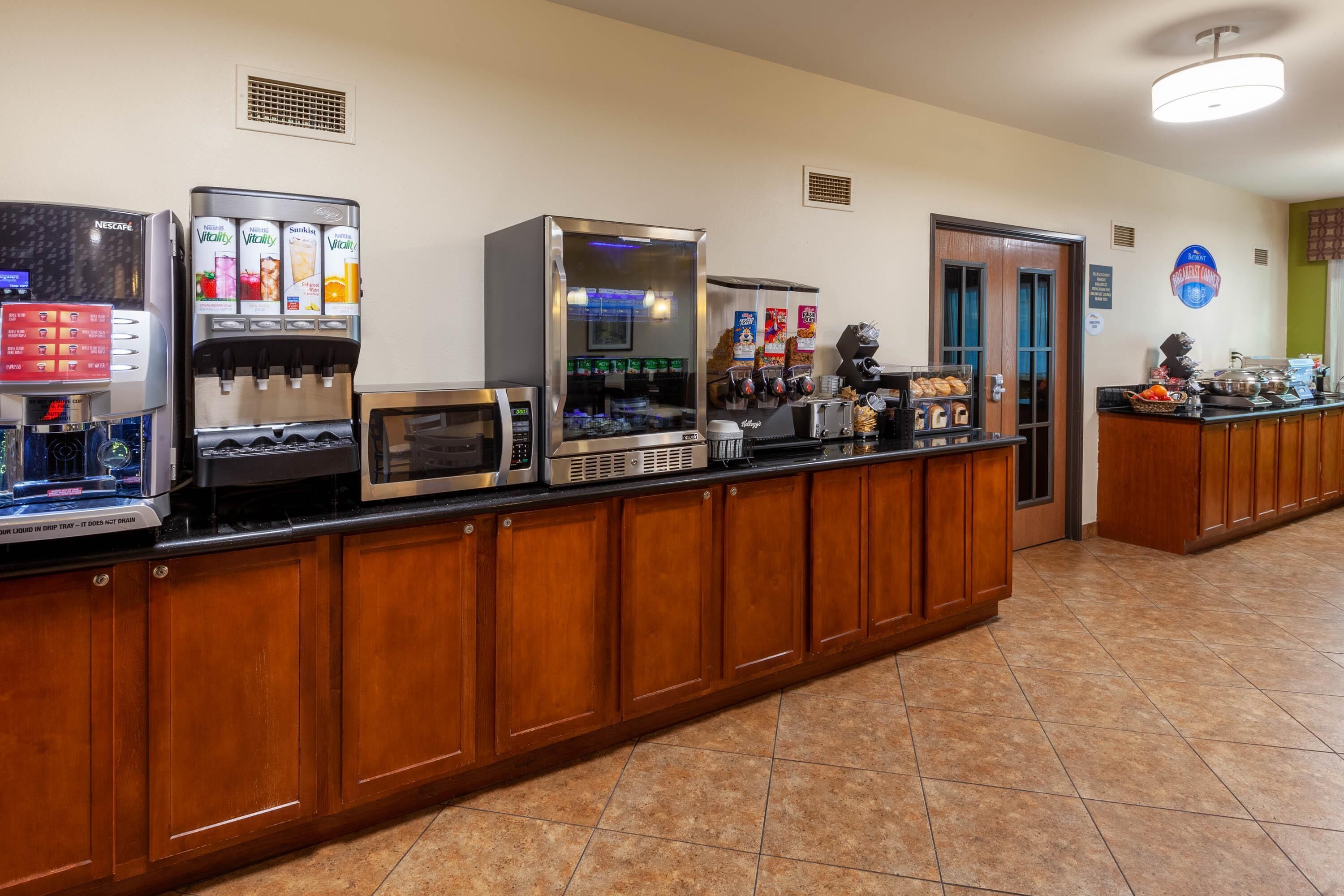 A hotel reception area with a coffee machine, a microwave, a refrigerator, and a counter with food items.